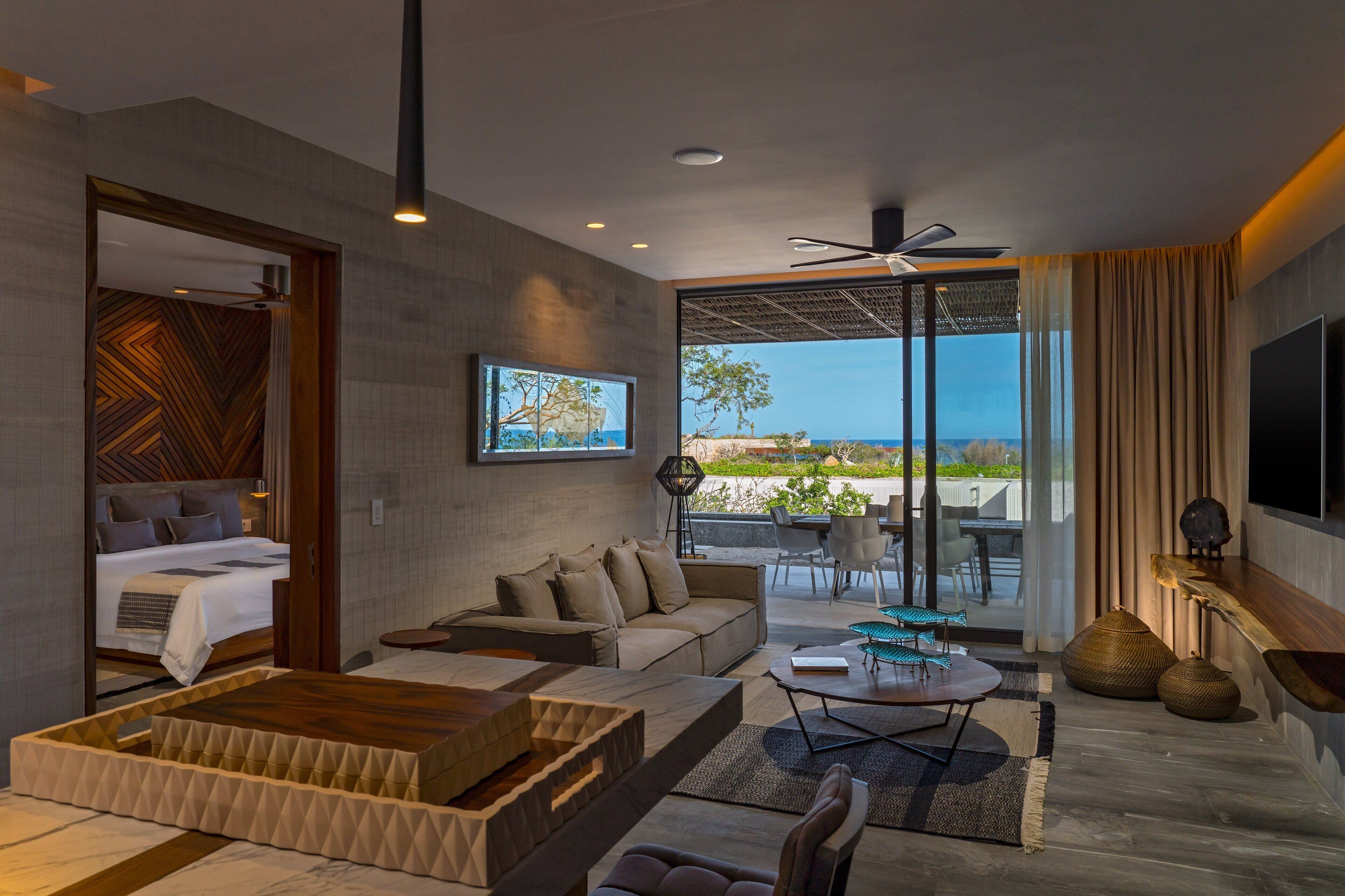 Una habitación de hotel moderna con cama, sofá, mesa de centro y balcón con vistas.
