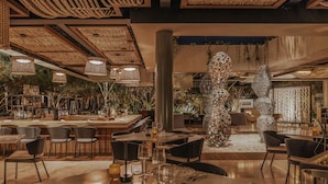 A restaurant with a modern interior, featuring wicker furniture, hanging lights, and a central decorative column. - Solaz, A Luxury Collection Resort, Los Cabos a Marriott Hotel (San José del Cabo)