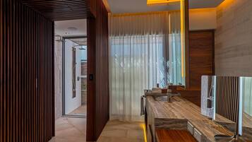 Un baño moderno con tocador de madera, un espejo grande y una zona de ducha visible a través de una puerta de vidrio.