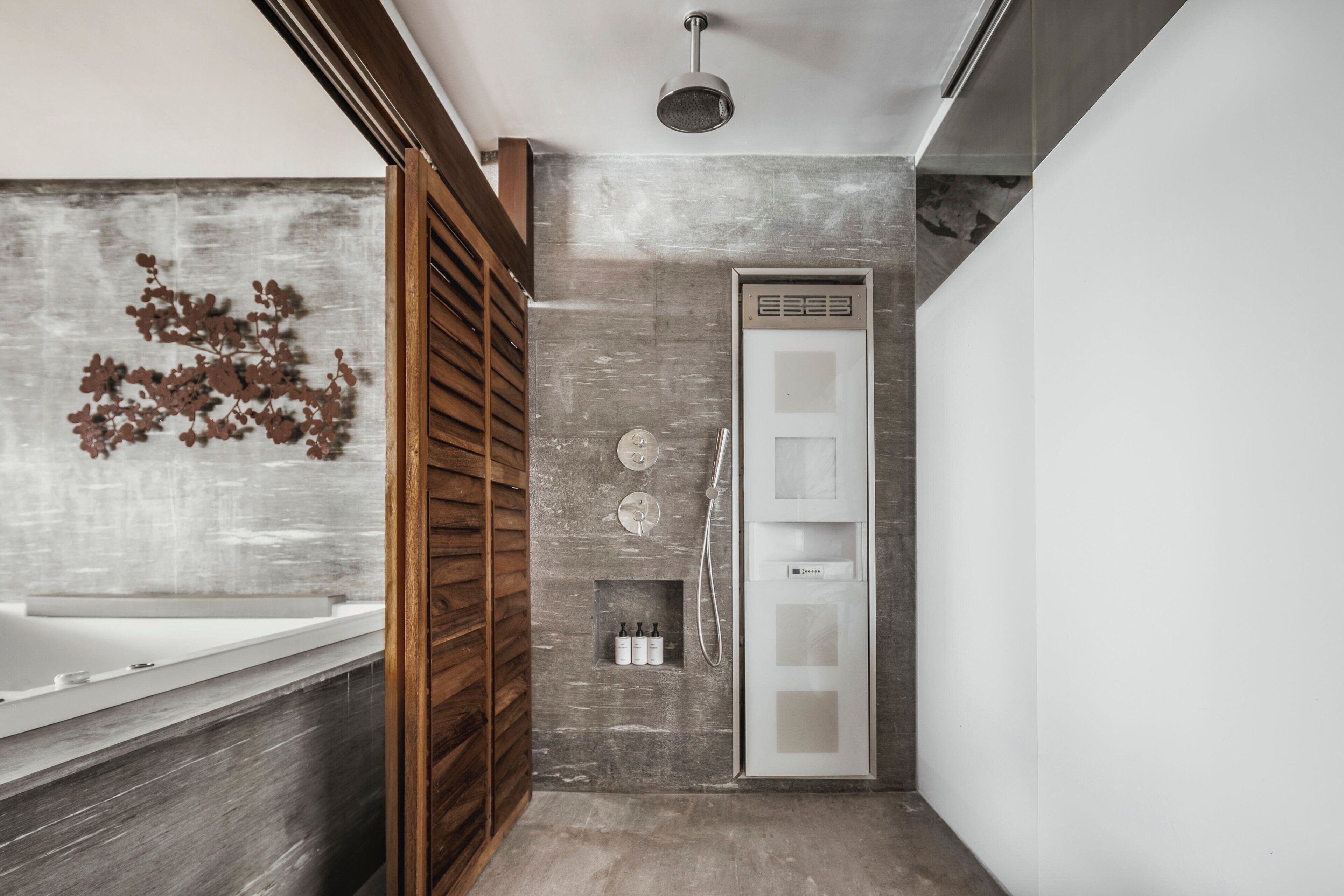 Une salle de bain moderne avec une porte à lattes en bois, une baignoire blanche et un espace douche doté d’un panneau de commande.