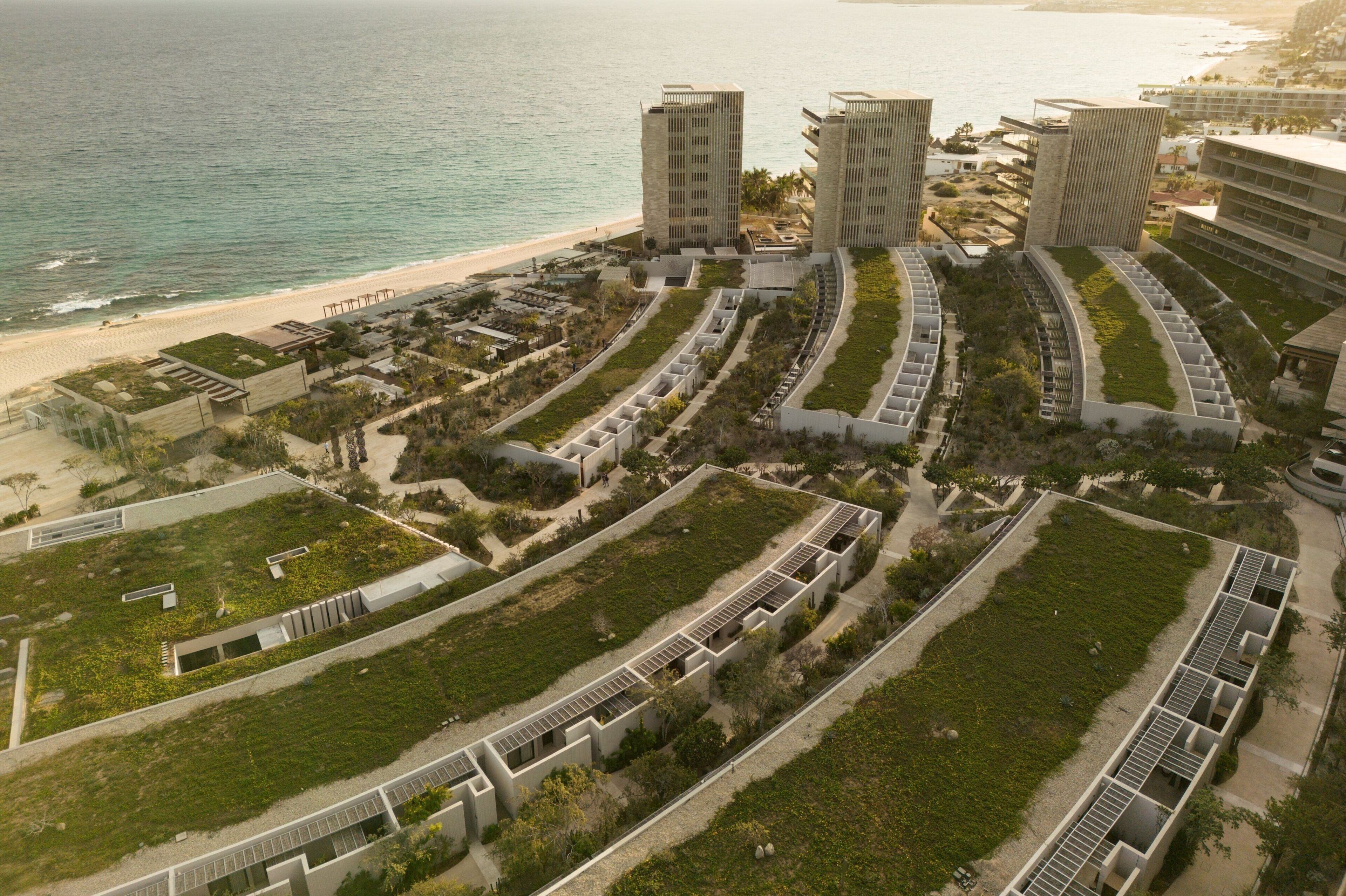 Vista aérea de un hotel costero con varias edificaciones, una playa y un jardín ajardinado.