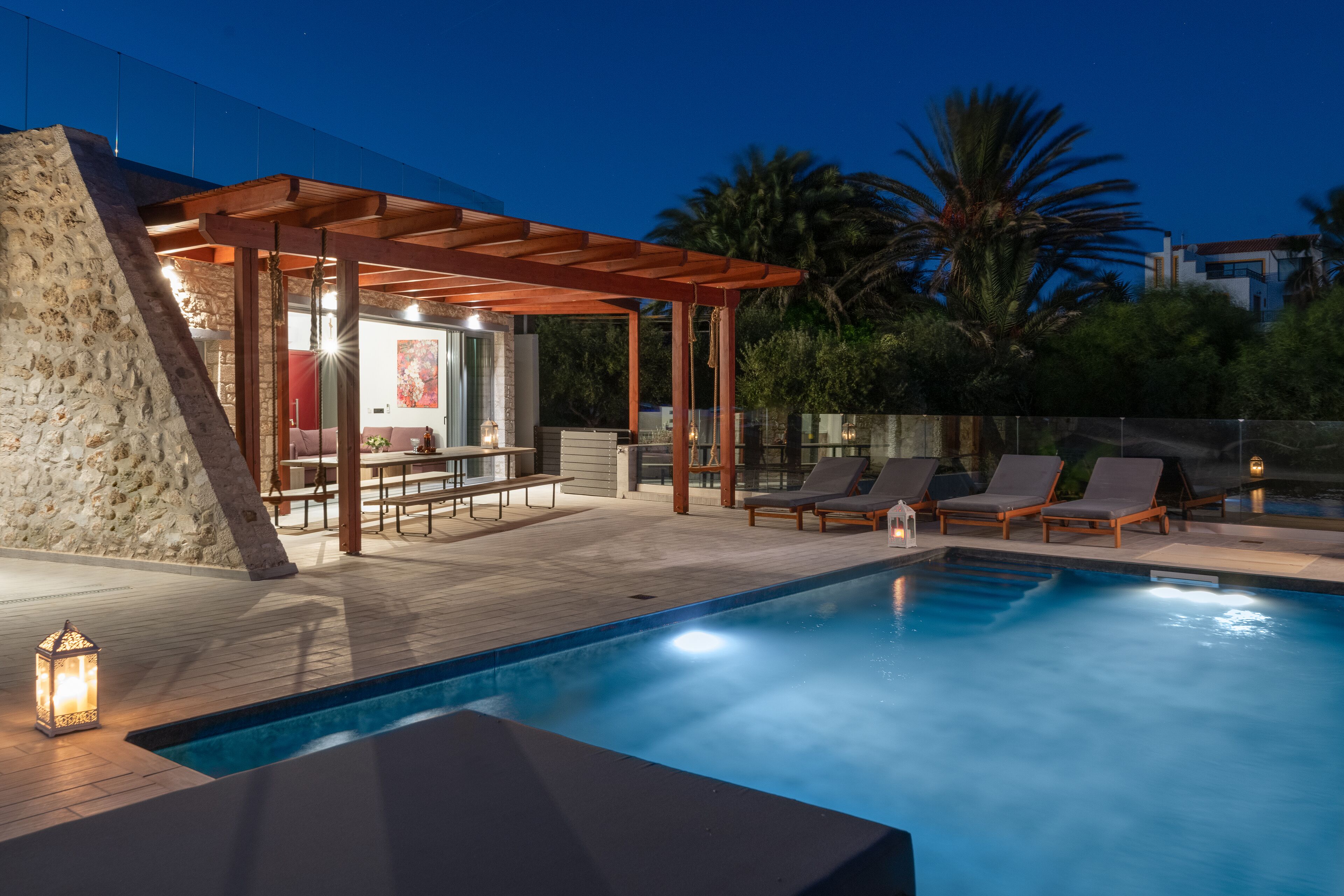 A pool area with lounge chairs, a pergola, and a stone wall.