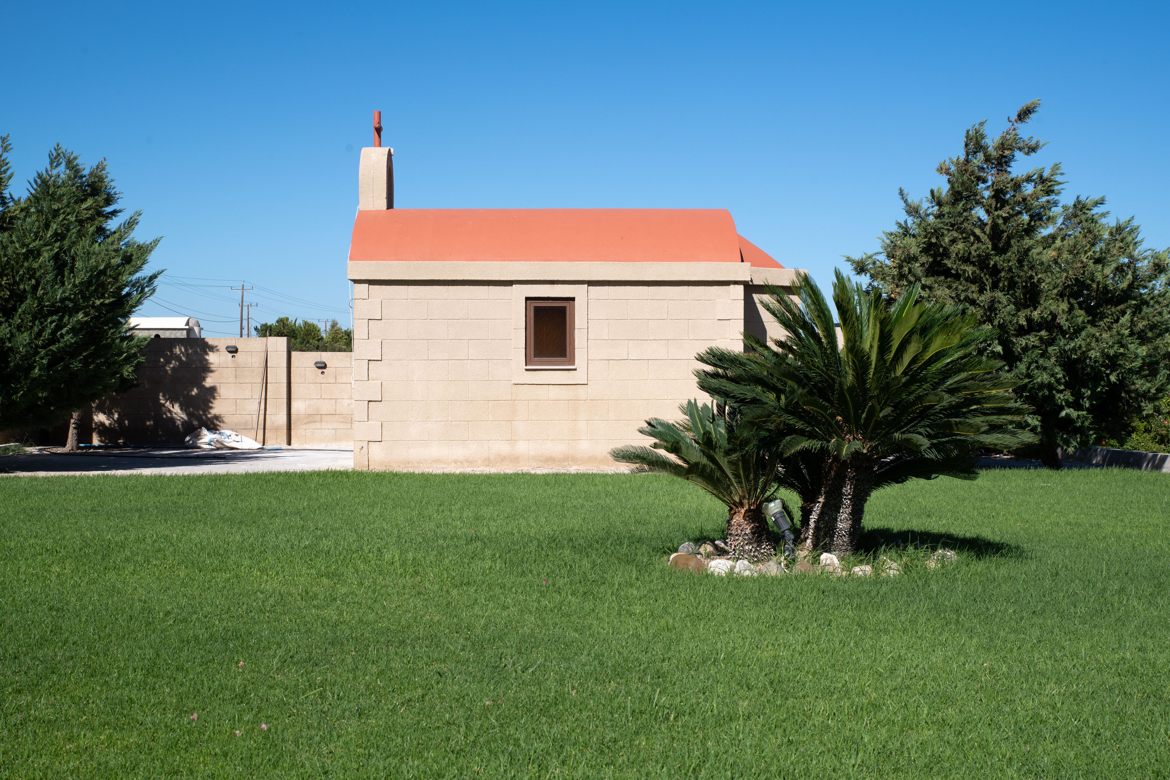A small, single-story building with a red roof, surrounded by a well-maintained lawn and a few trees.