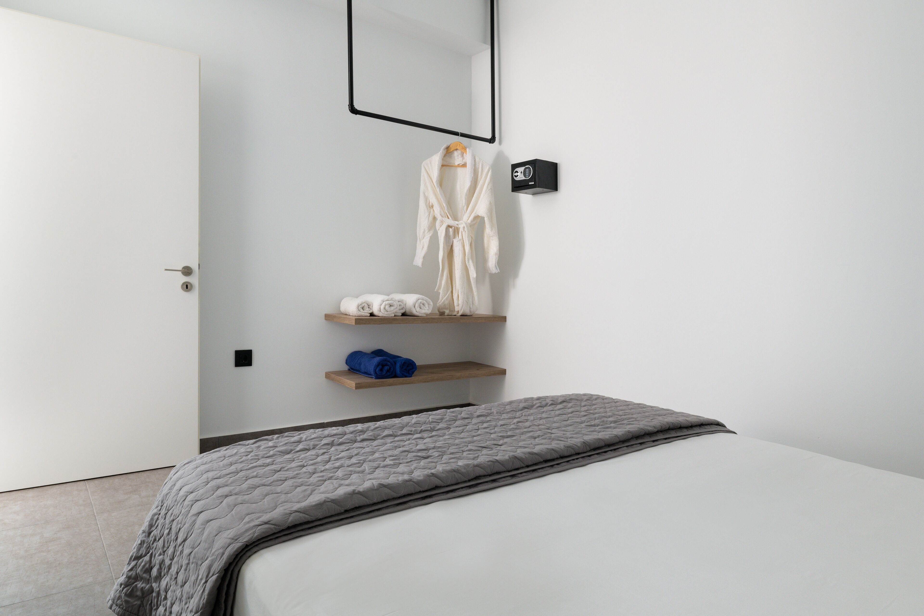 Un dormitorio minimalista con una cama, una bata y un estante con toallas.