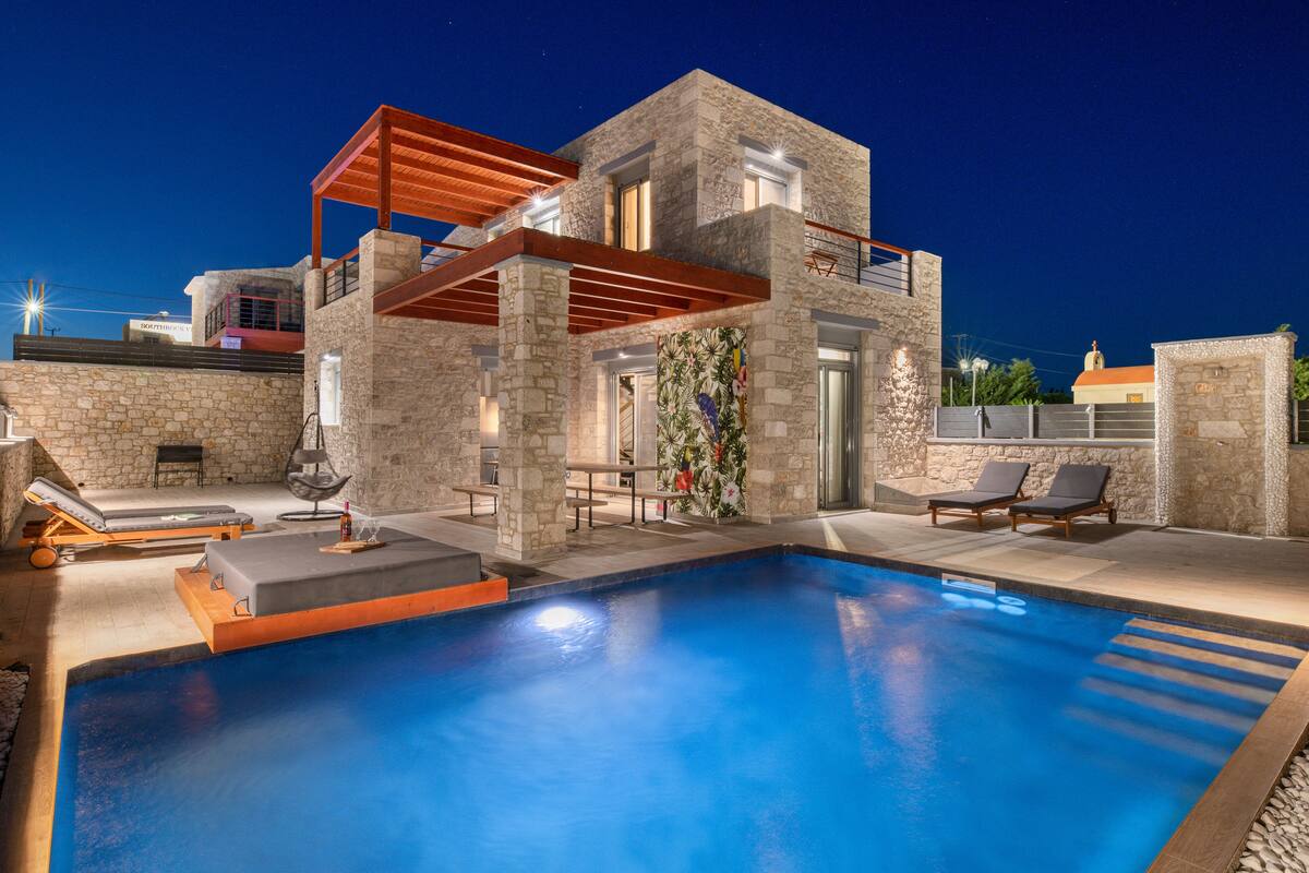 A modern house with a swimming pool, stone walls, and a wooden pergola.