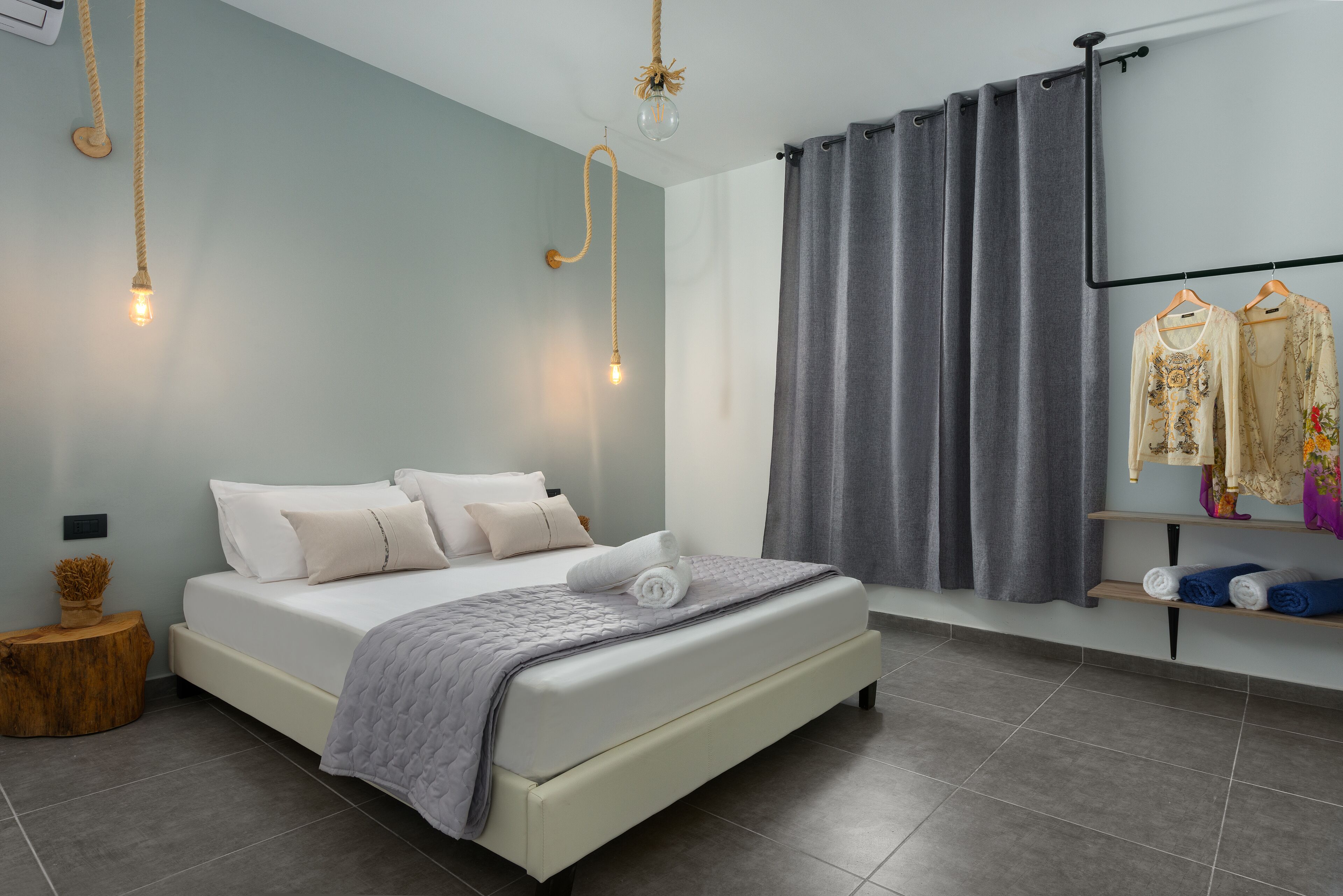 Een moderne slaapkamer met een bed, grijze gordijnen en een hanglamp.