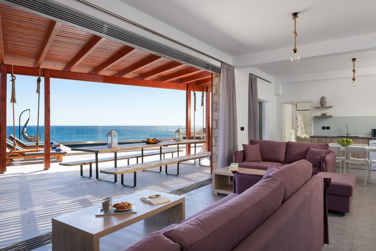 A spacious living area with a large sofa, a dining table, and a view of the ocean.