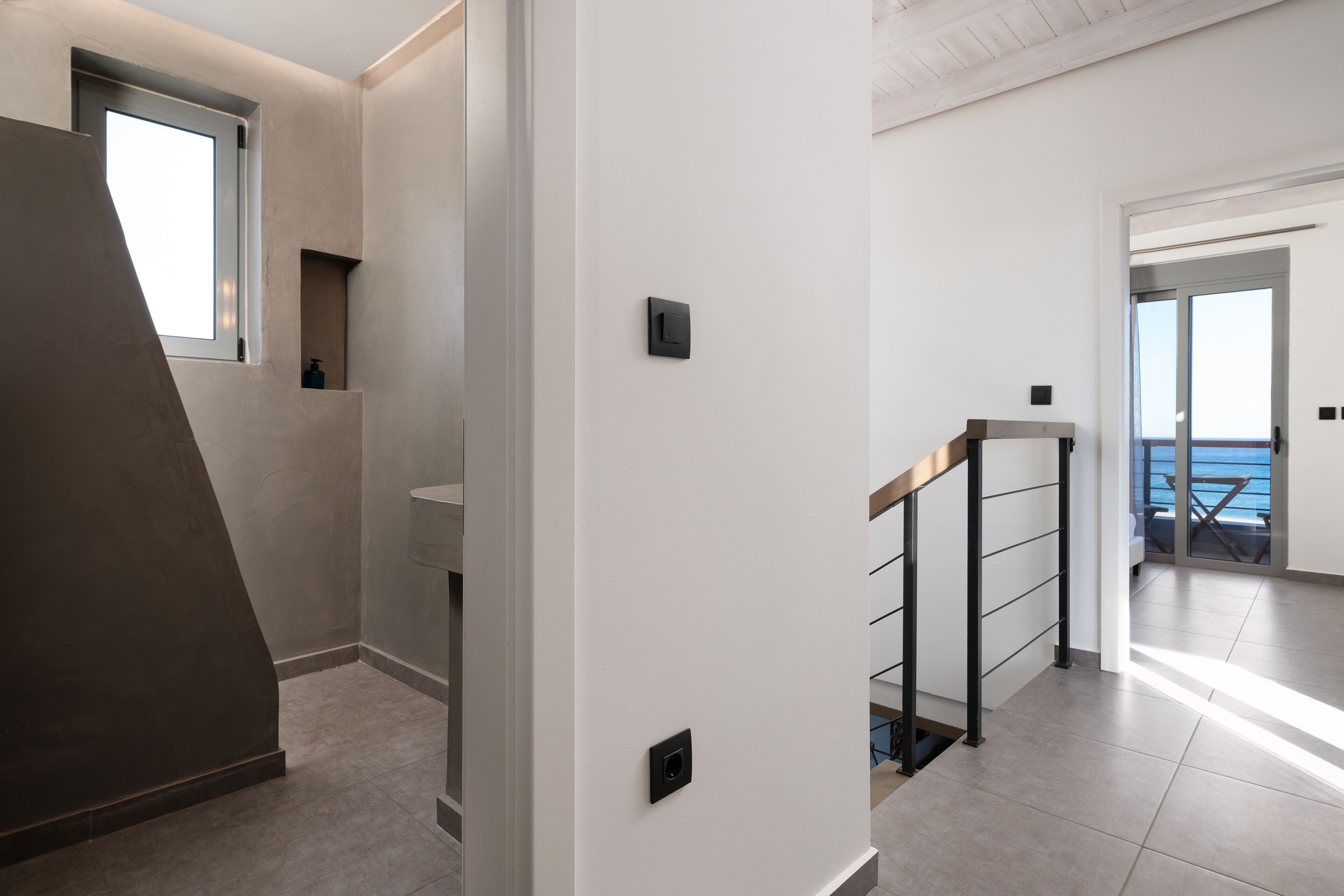A modern interior with a staircase, a small window, and a view of the sea.