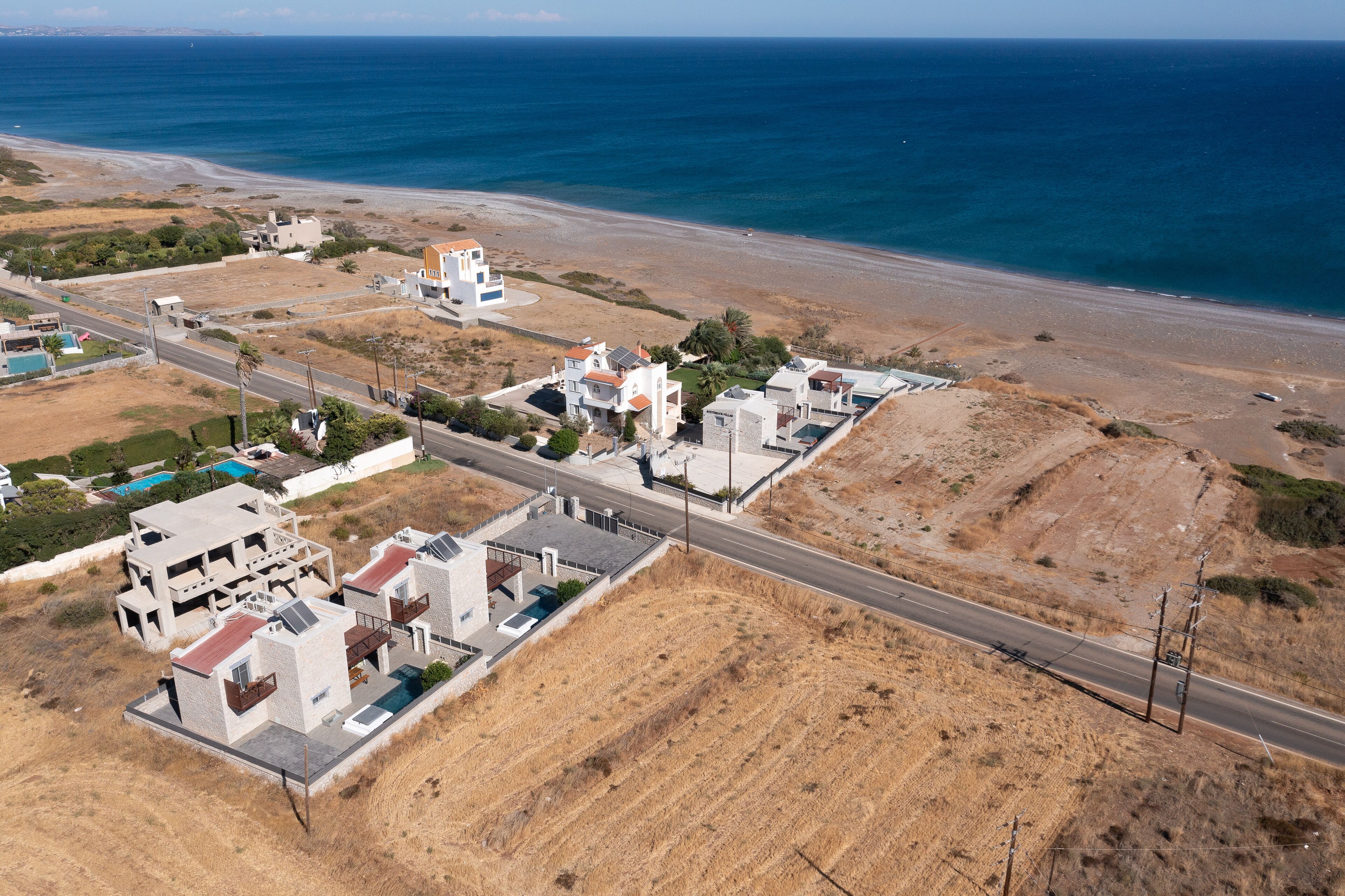 An aerial view of a coastal residential area with modern houses, a road, and a beach.