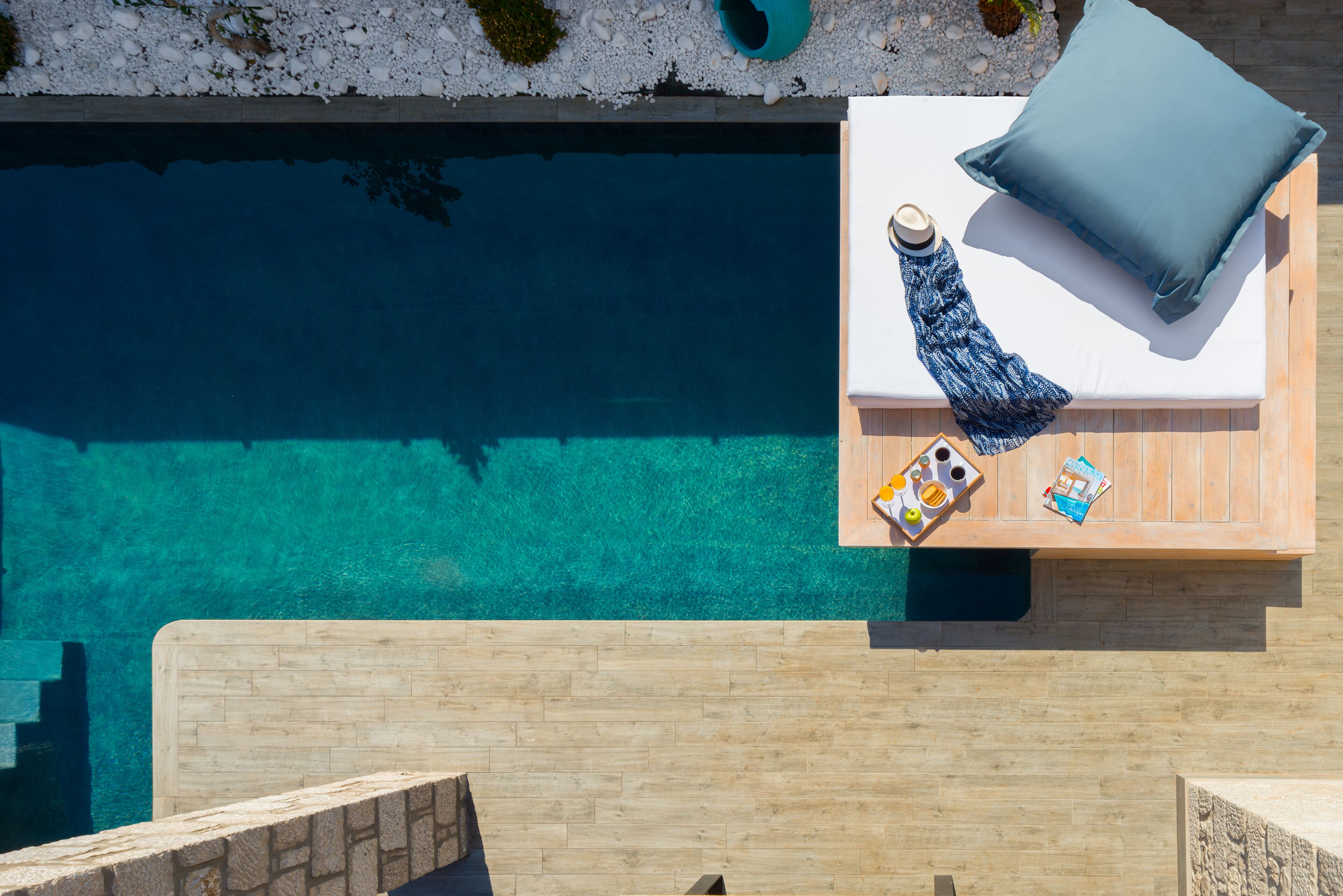 A poolside area with a wooden deck, a lounge chair with a cushion, and a small table with a towel and a bottle.