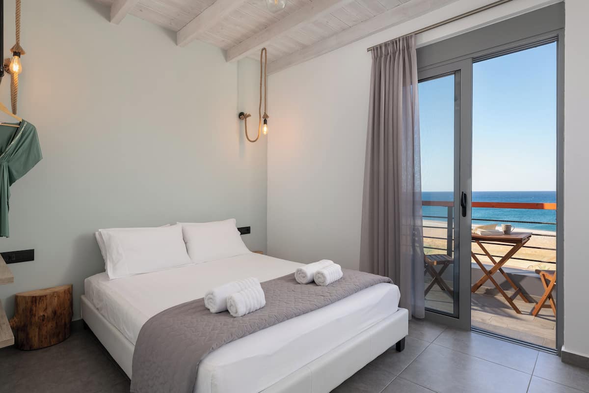 A bedroom with a bed, a view of the beach, and a table by the window.