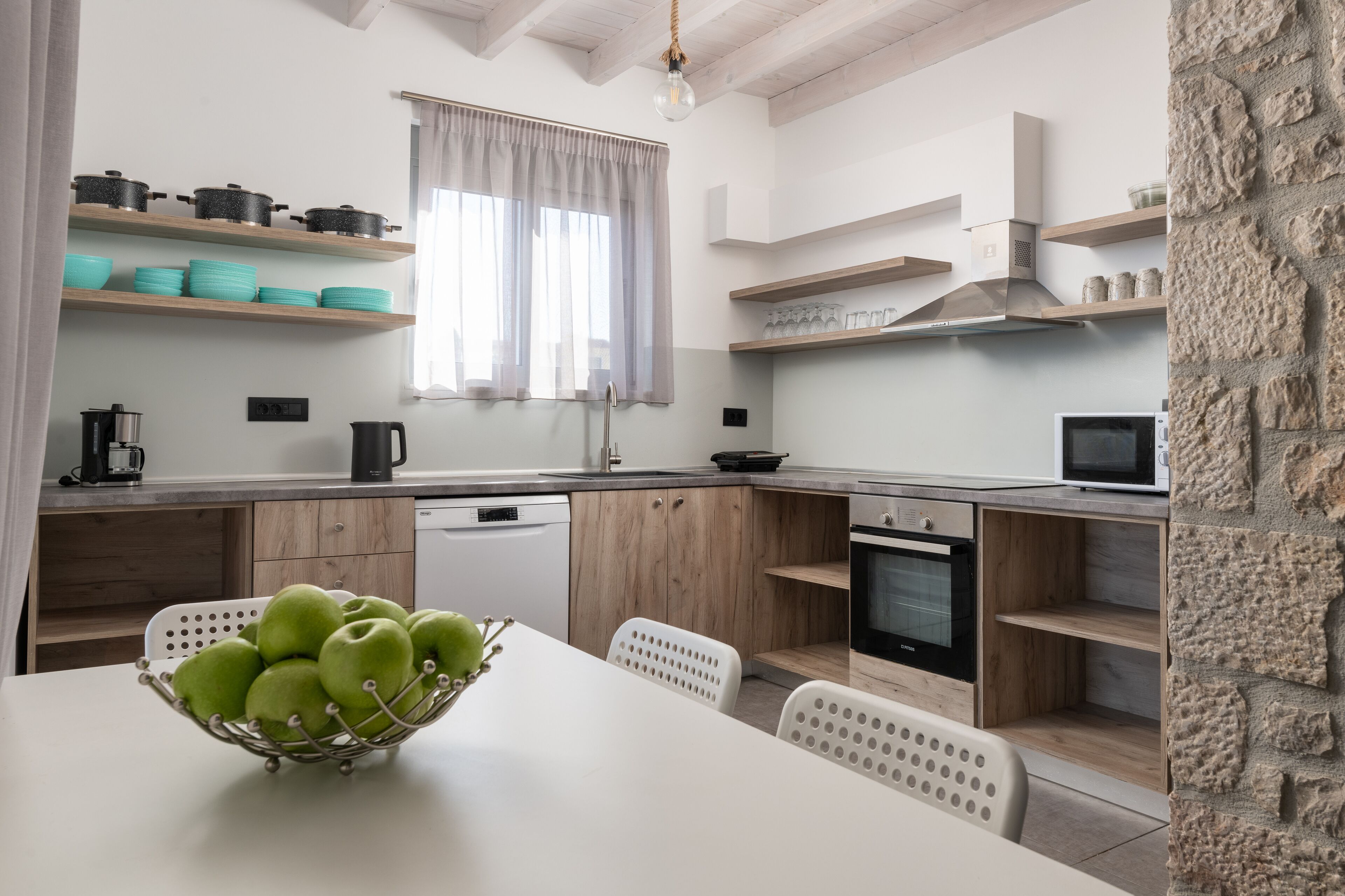 A modern kitchen with wooden cabinets, a dining table with a bowl of green apples, and a stone accent wall.