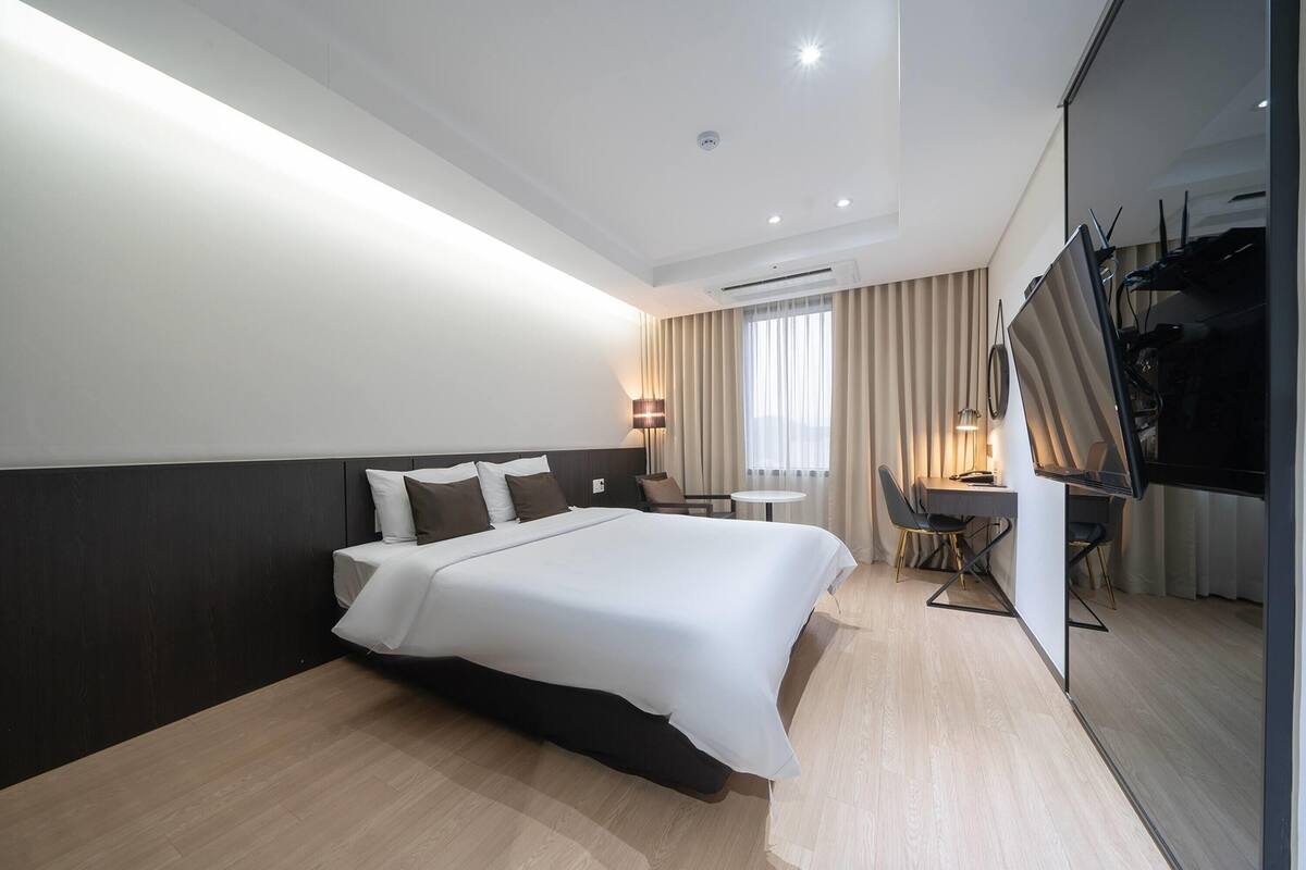 A modern hotel room with a large bed, a desk, and a TV.