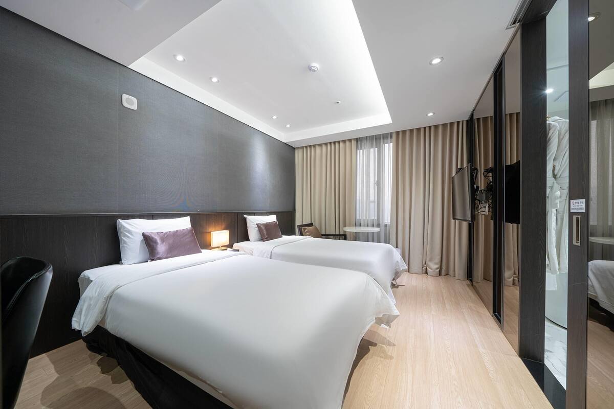 A hotel room with two beds, a desk, a chair, a TV, and a window with curtains.