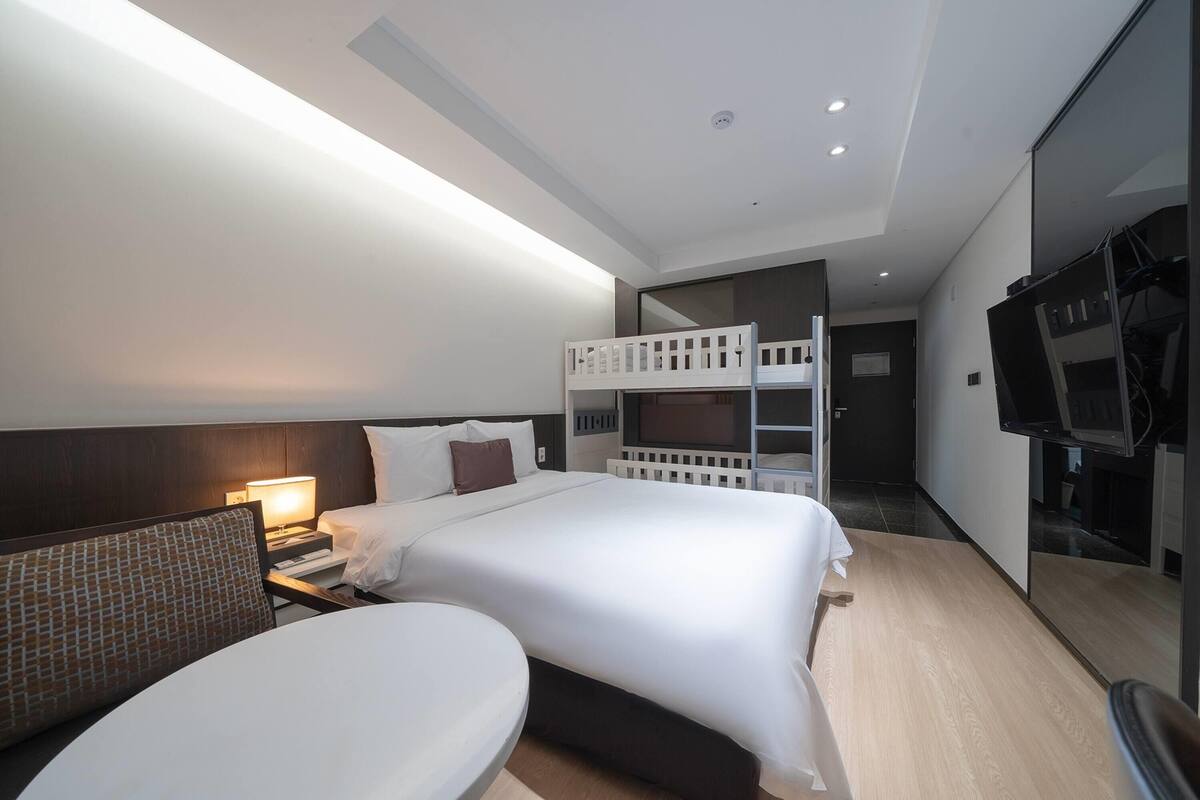 A modern hotel room with a large bed, a desk, a chair, a TV, and a balcony.