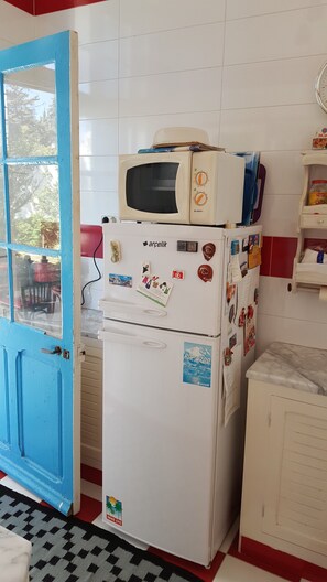 Una cocina compacta con un refrigerador blanco, un microondas encima y una puerta azul.