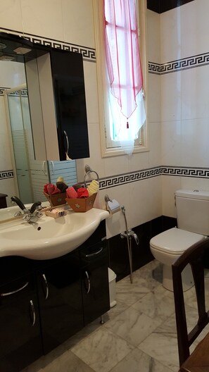 A bathroom with a white sink, a mirror, a toilet, and a window with a pink curtain.