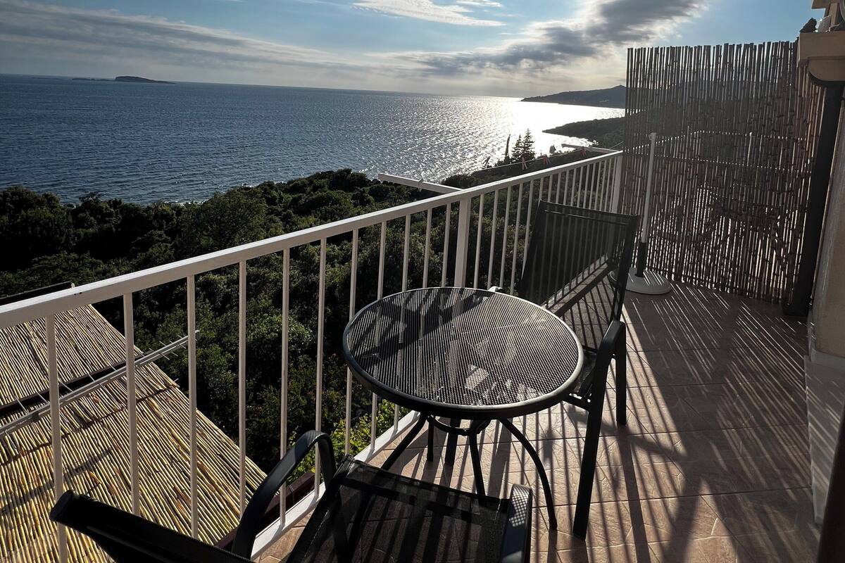 A balcony with a table and chairs overlooking a body of water and a distant island.