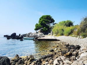 A rocky shoreline with a boat docked near the water, a tree, and a small dock.