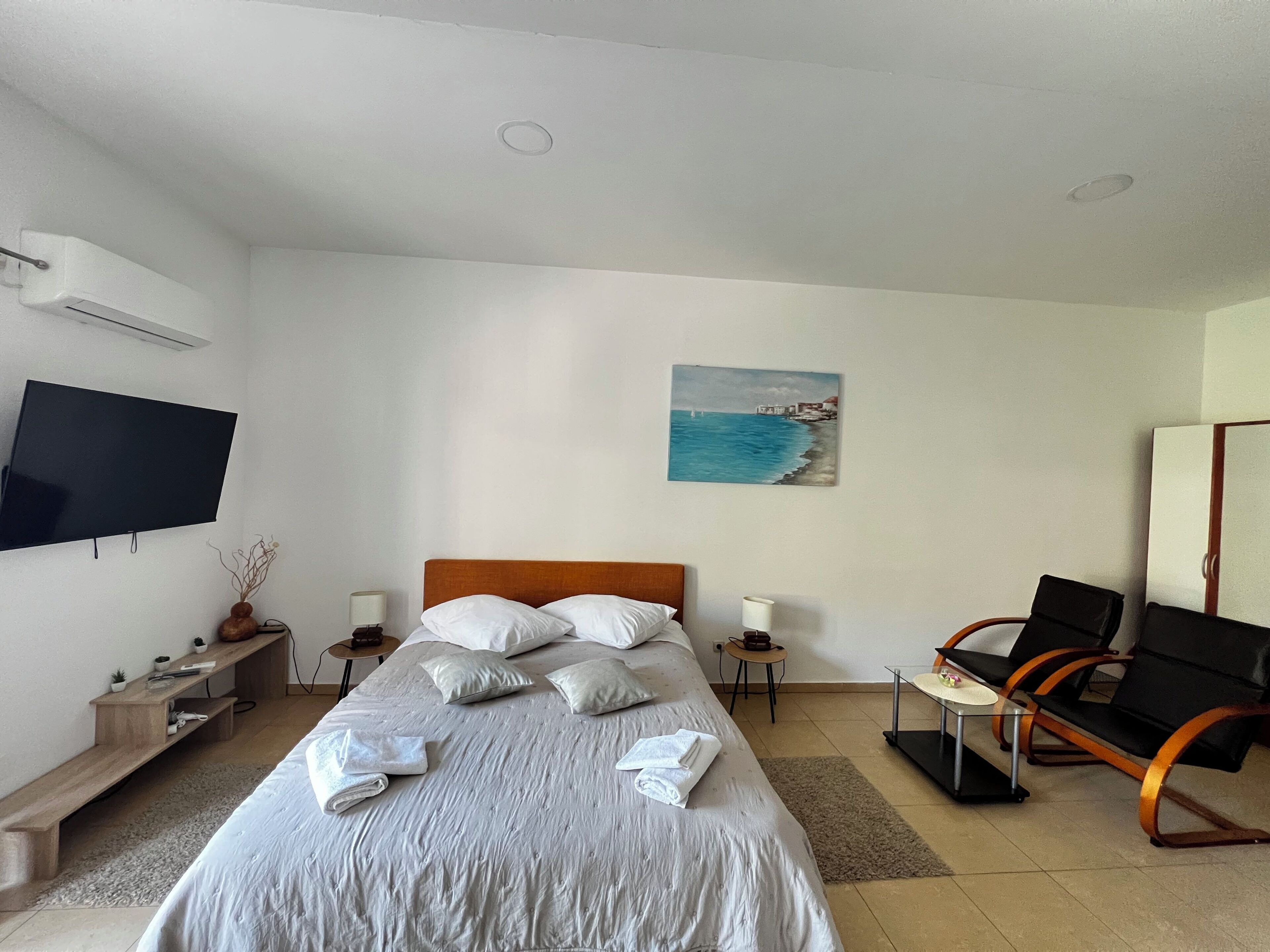 Ein Hotelzimmer mit Bett, Fernseher, Gemälde, Schreibtisch und Stuhl.