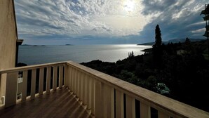 Ein Balkon mit Blick auf das Meer und das entfernte Land unter einem teils bewölkten Himmel.