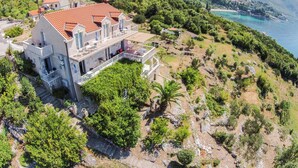 Ein großes, mehrstöckiges Haus mit rotem Ziegeldach, mehreren Balkonen und Blick auf das Meer.