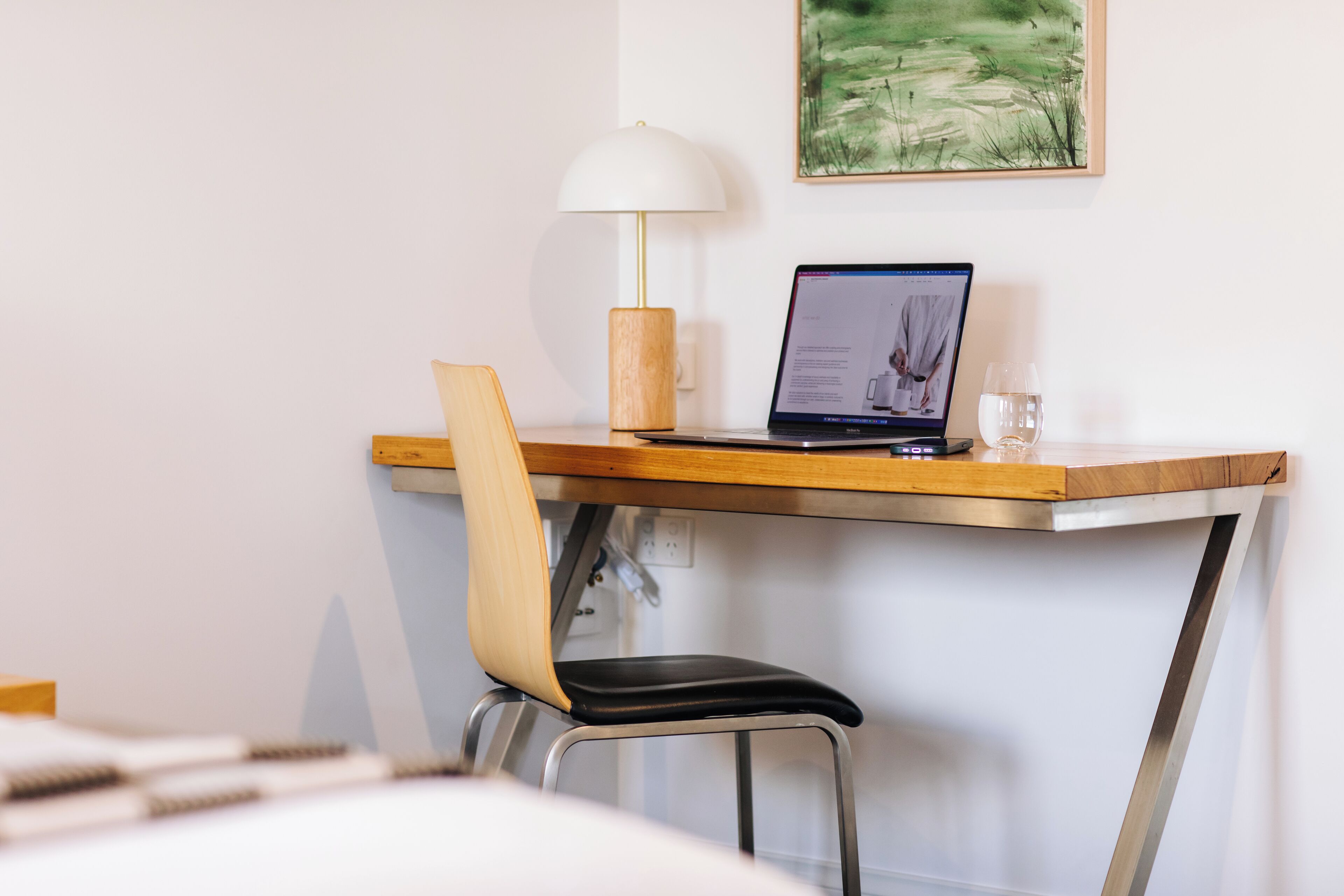 A modern workspace with a laptop, a wooden desk, a metal chair, and a white lamp.
