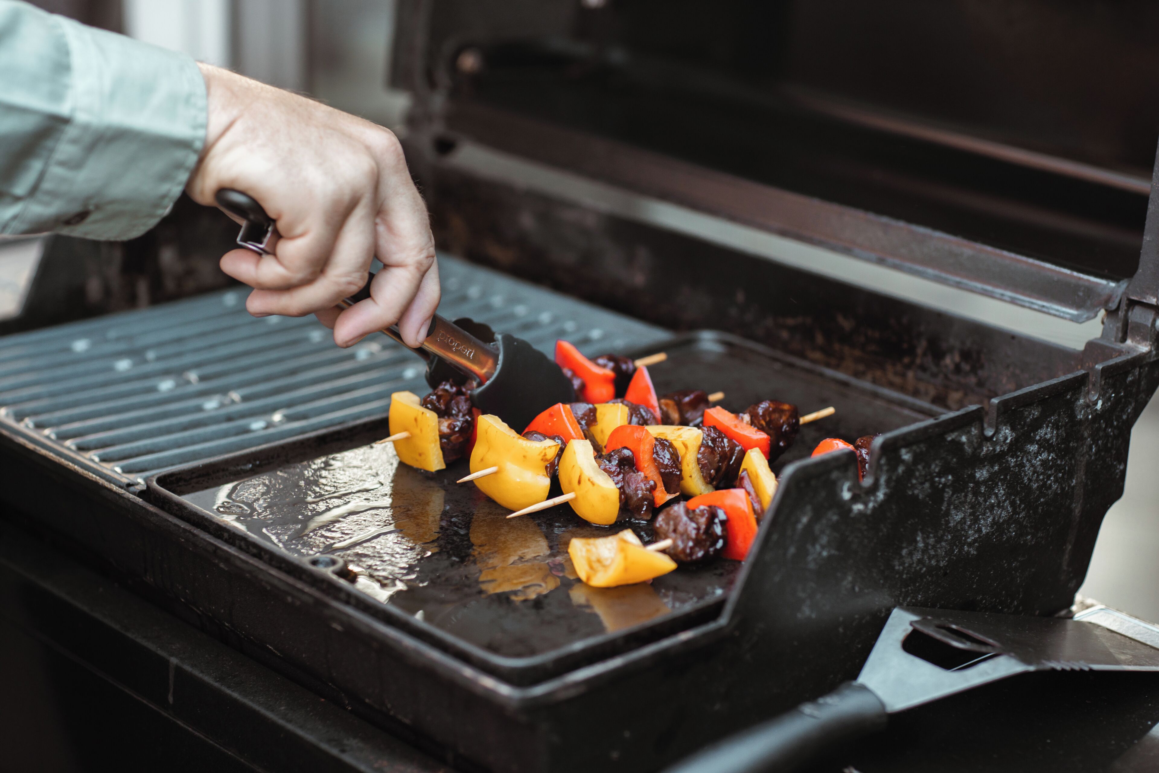 A hand grilling skewers of meat and vegetables on a grill.