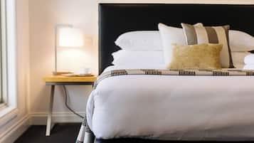 Ein ordentlich bezogenes Bett mit weißer Bettwäsche und gestreifte Kissen, ein Nachttisch mit einer Lampe und ein Fenster auf der linken Seite.