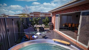 Un patio trasero con jacuzzi, muebles de jardín y una casa de ladrillo.