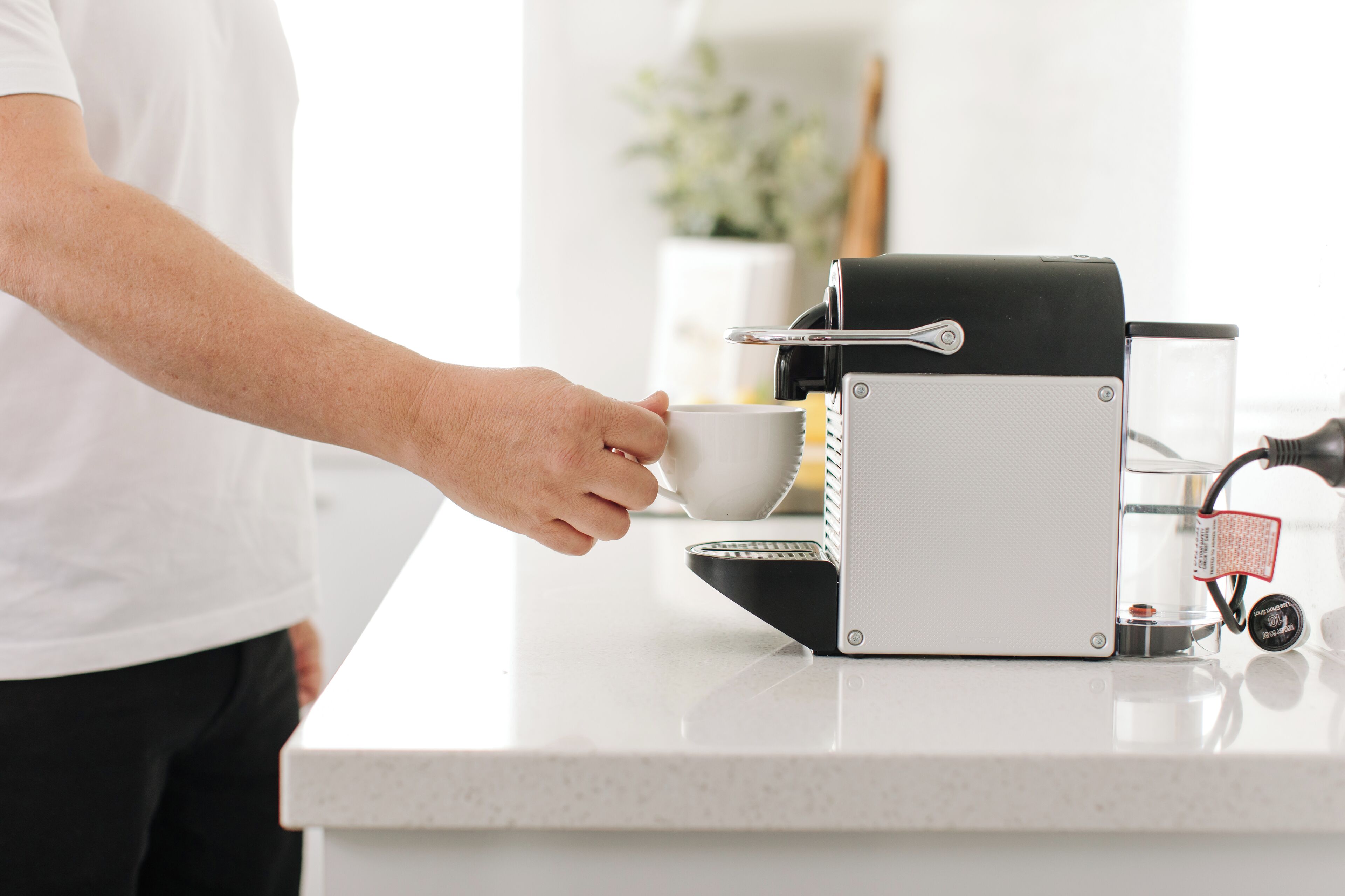 Una persona sosteniendo una taza cerca de una máquina de café sobre una encimera.