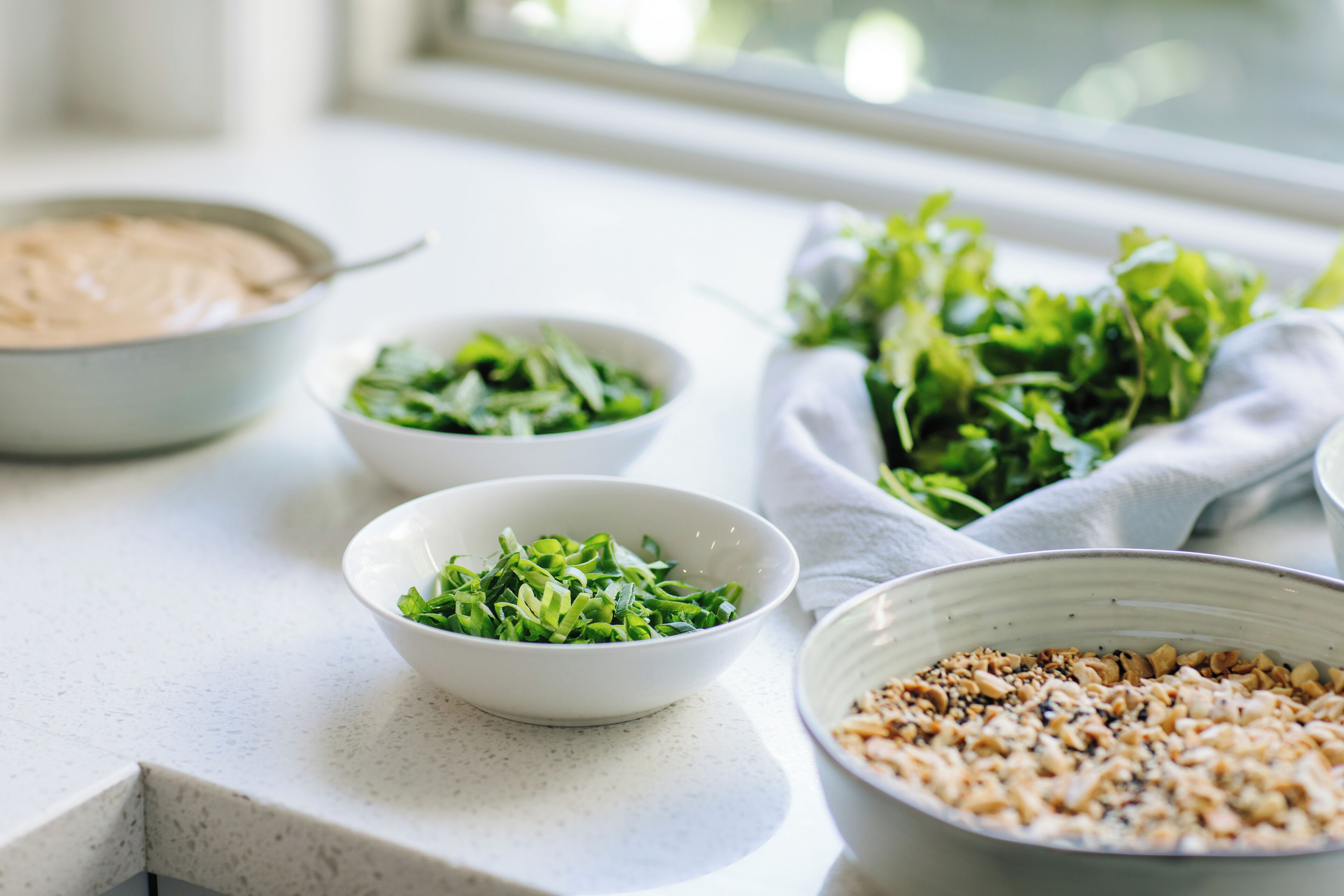 Una encimera de cocina con recipientes que contienen verduras, frutos secos y una sustancia cremosa.