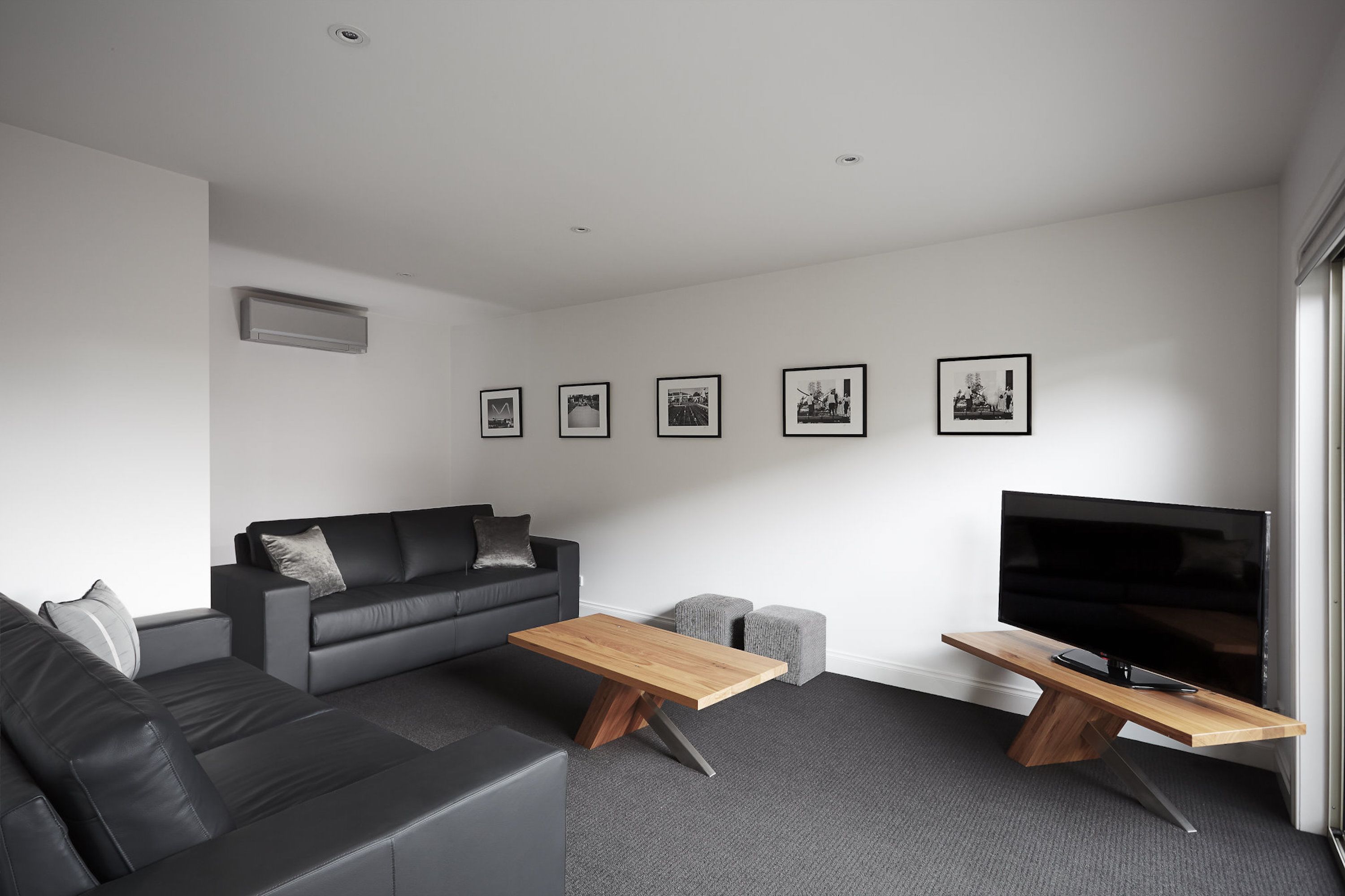 Una sala de estar moderna con un sofá de cuero negro, una mesa de centro de madera, un televisor de pantalla plana y una alfombra gris.