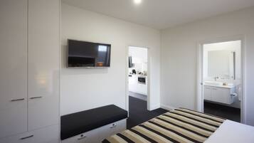 Une chambre d’hôtel moderne équipée d’un lit, d’un téléviseur fixé au mur, d’une salle de bain avec un miroir et d’un coin cuisine.