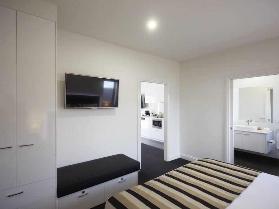 Une chambre d’hôtel moderne équipée d’un lit, d’un téléviseur fixé au mur, d’une salle de bain avec un miroir et d’un coin cuisine.