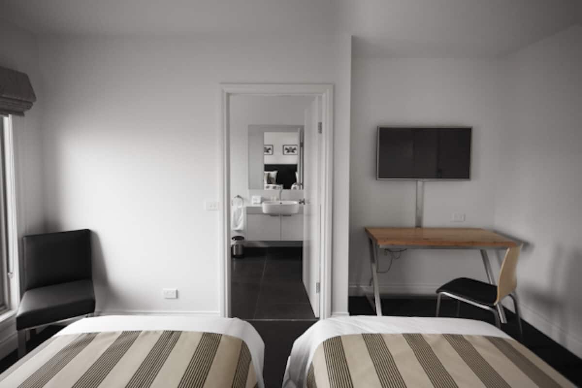 Habitació d'hotel amb dos llits, un escriptori, una cadira, un televisor i un bany visible a través d'una porta oberta.