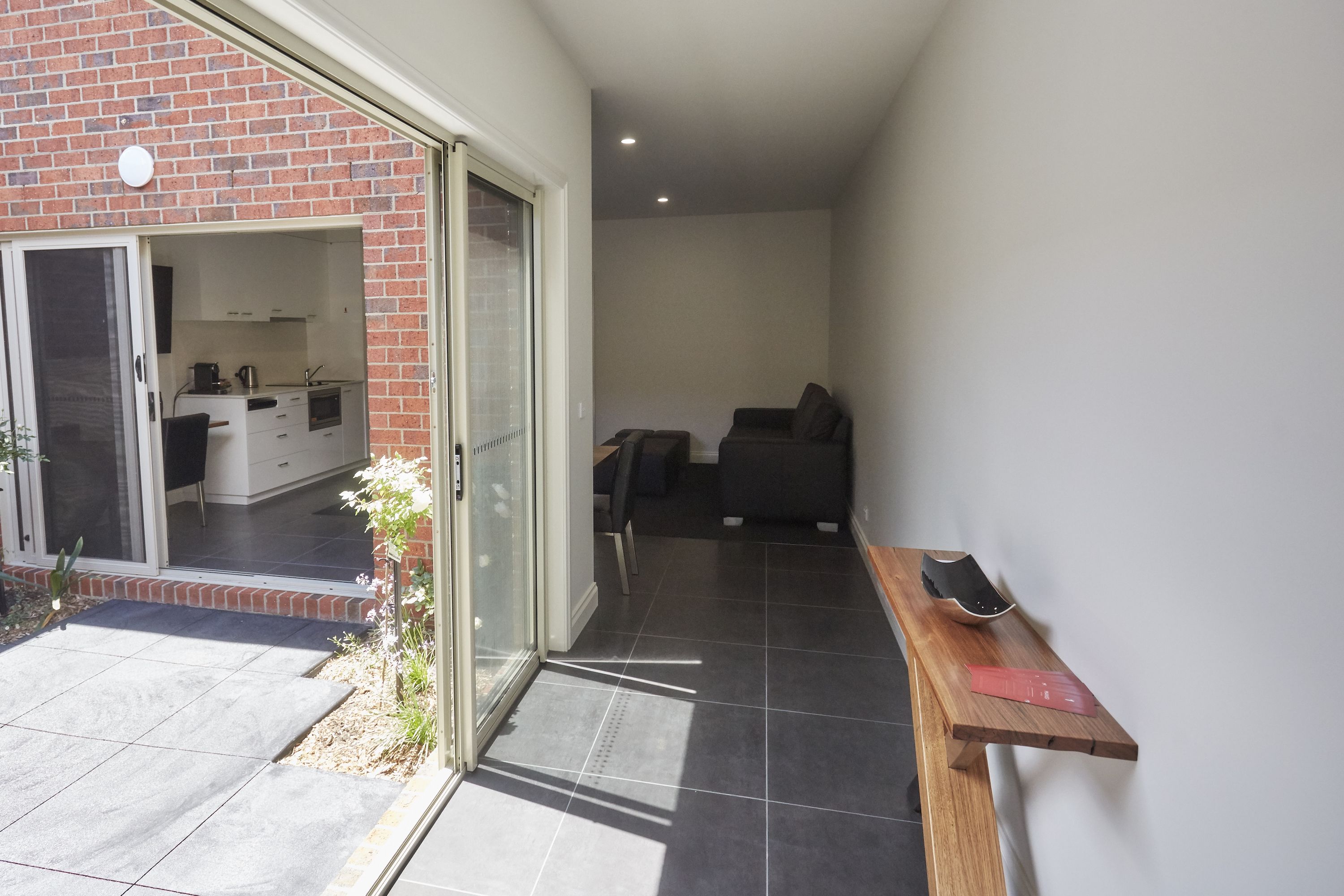 A modern kitchen with sliding doors, a dining area with a sofa, and a wooden table with a red object.