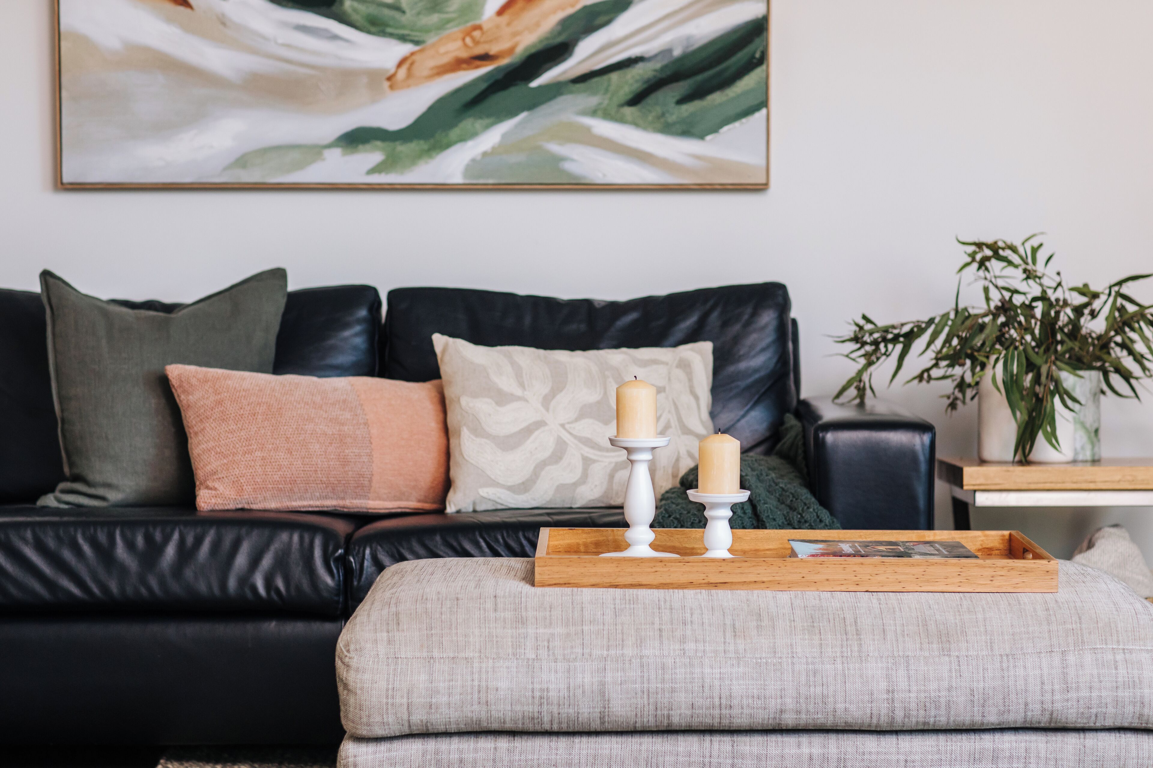 A living room with a black leather sofa, a grey armchair, and a wooden tray with candles.