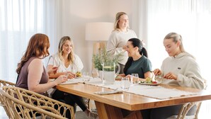 Un grupo de personas cenando en una mesa de madera, con una jofaina de agua y una planta en el centro.