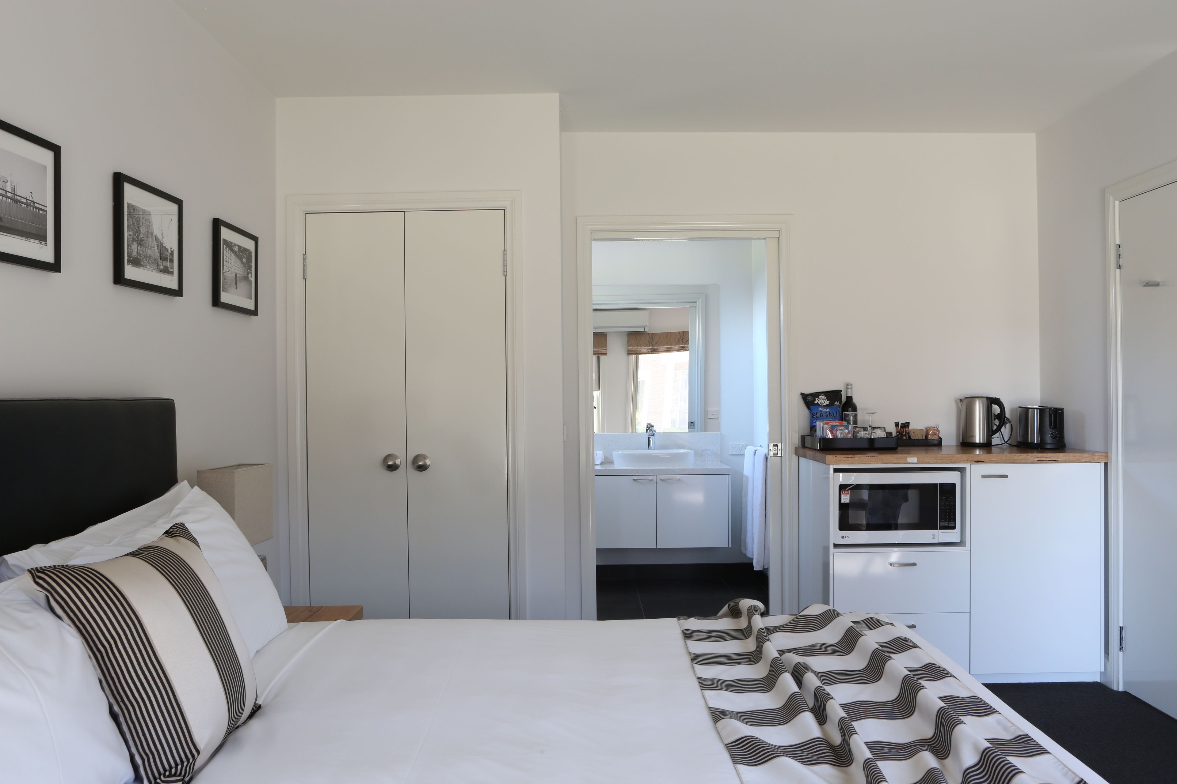 A hotel room with a bed, a desk with a microwave, a sink, and a door leading to a bathroom.