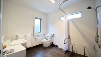 A modern bathroom with a sink, toilet, and shower. It includes a window, a towel rack, and a grab bar for safety.