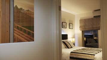 Een hotelkamer met een bed, een raam met uitzicht op een houten constructie, een nachtkastje met een lamp, en een raam met een blind.