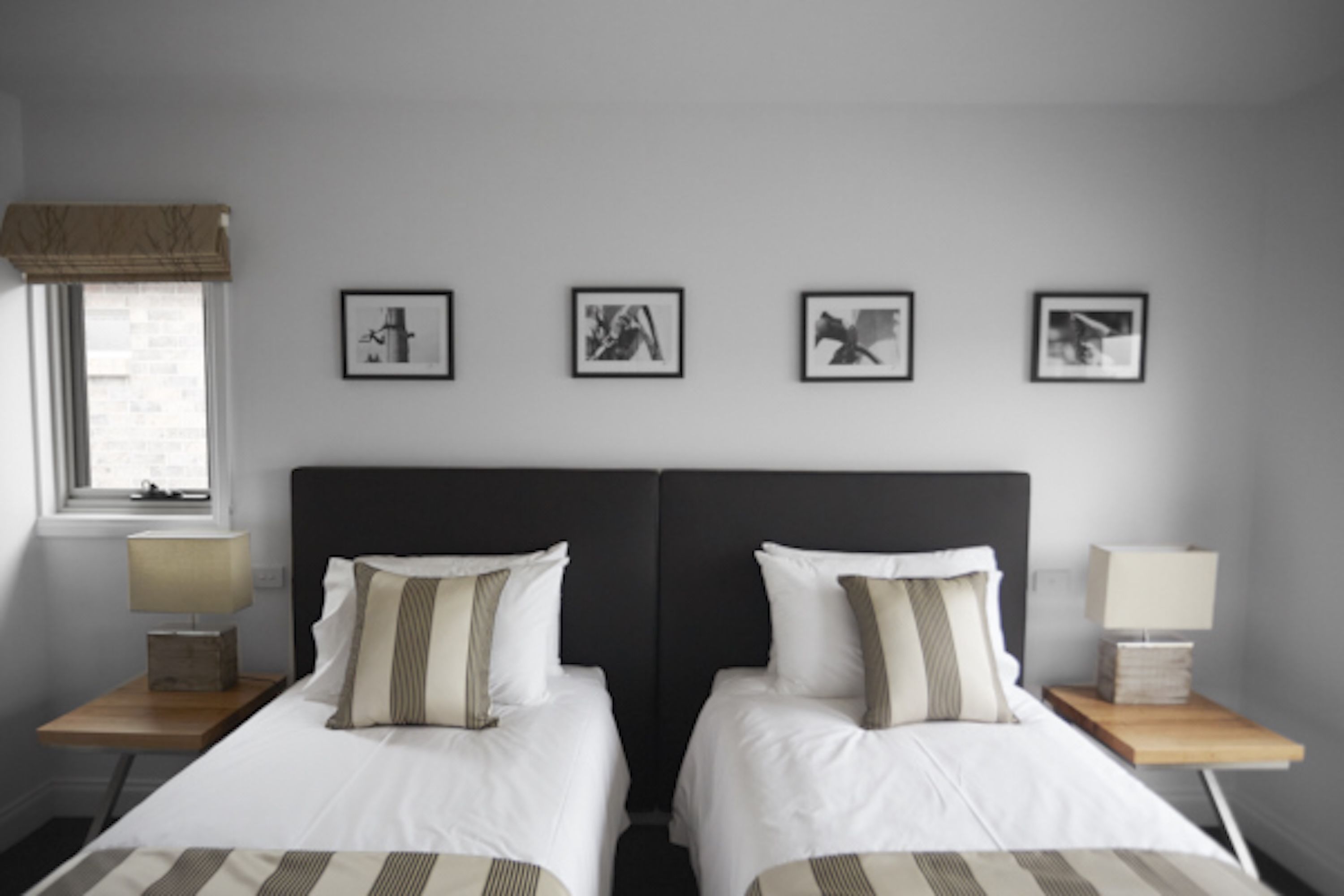 A hotel room with two beds, a window with a view, and four framed pictures on the wall.