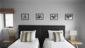 A hotel room with two beds, a window with a view, and four framed pictures on the wall.