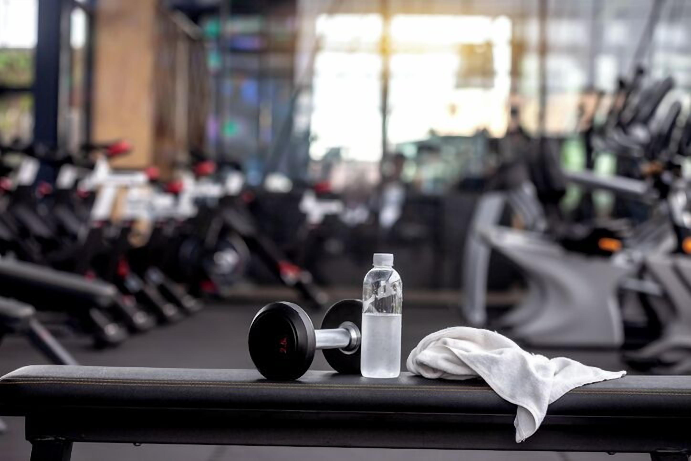 A gym with exercise equipment, a water bottle, and a towel on a bench.