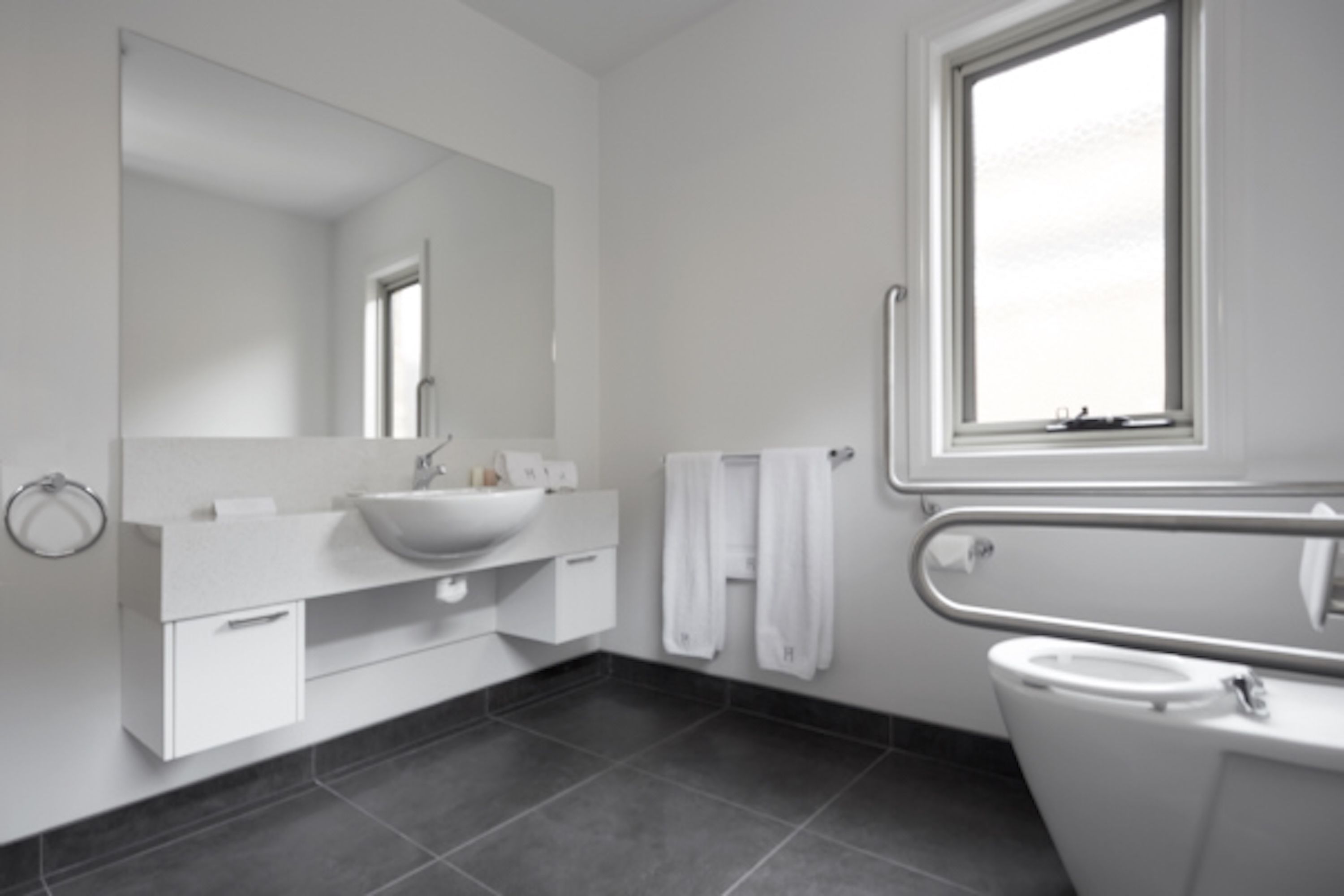 Une salle de bain moderne avec un grand miroir, un lavabo blanc et une fenêtre située au-dessus des toilettes.