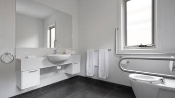 A modern bathroom with a large mirror, white sink, and a window above the toilet.