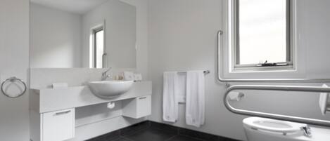 Une salle de bain moderne avec un grand miroir, un lavabo blanc et une fenêtre située au-dessus des toilettes.