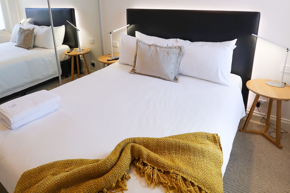 Habitació d'hotel amb un llit gran, un altre més petit, un mirall, un quadre i una làmpada.