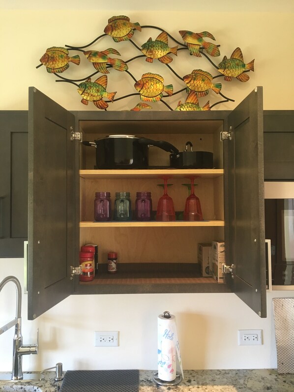 Un meuble de cuisine ouvert, avec des étagères contenant des bocaux, une bouilloire et une décoration murale représentant un poisson.